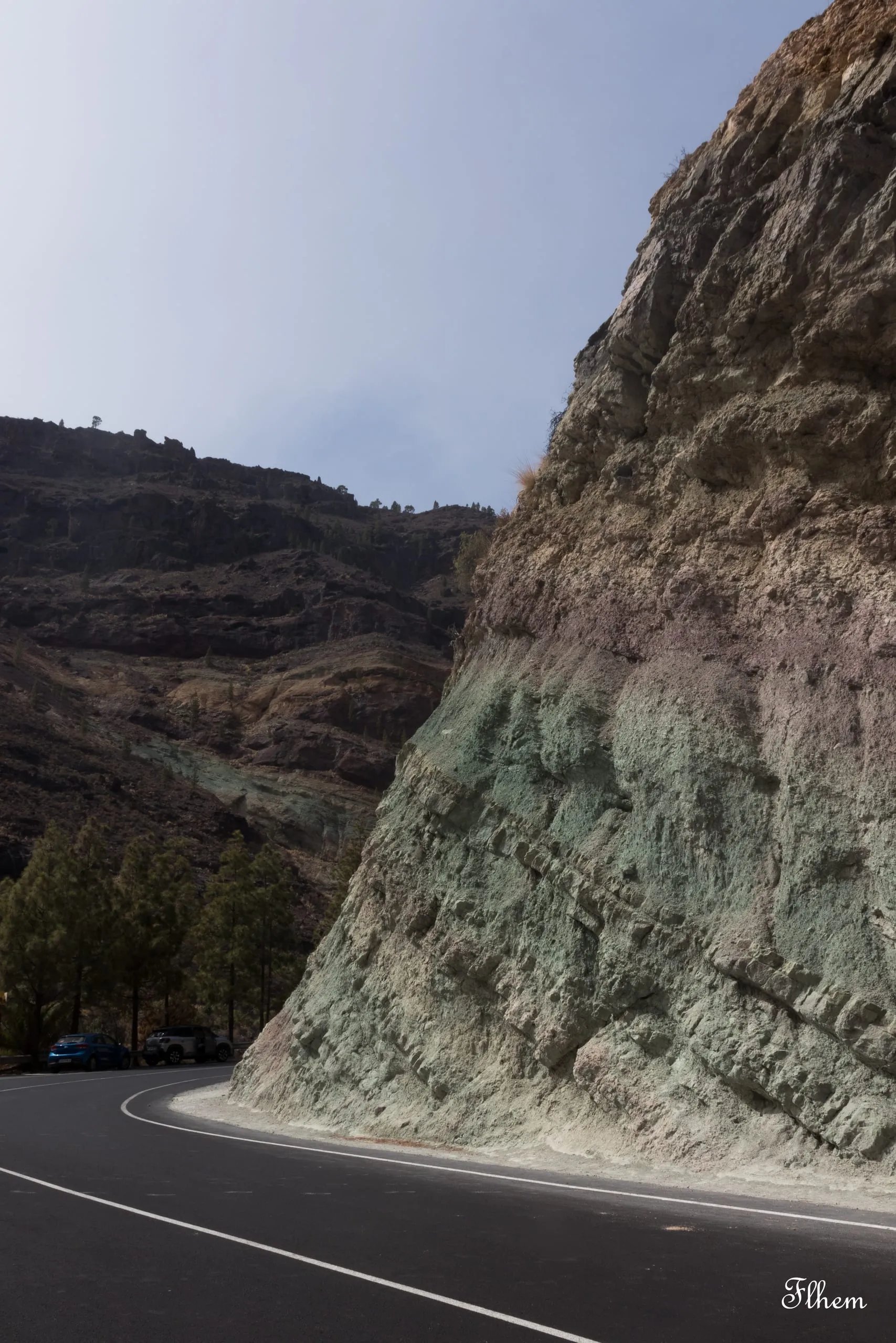 Route en lacet au pied d'une paroi rocheuse aux strates vertes et violettes