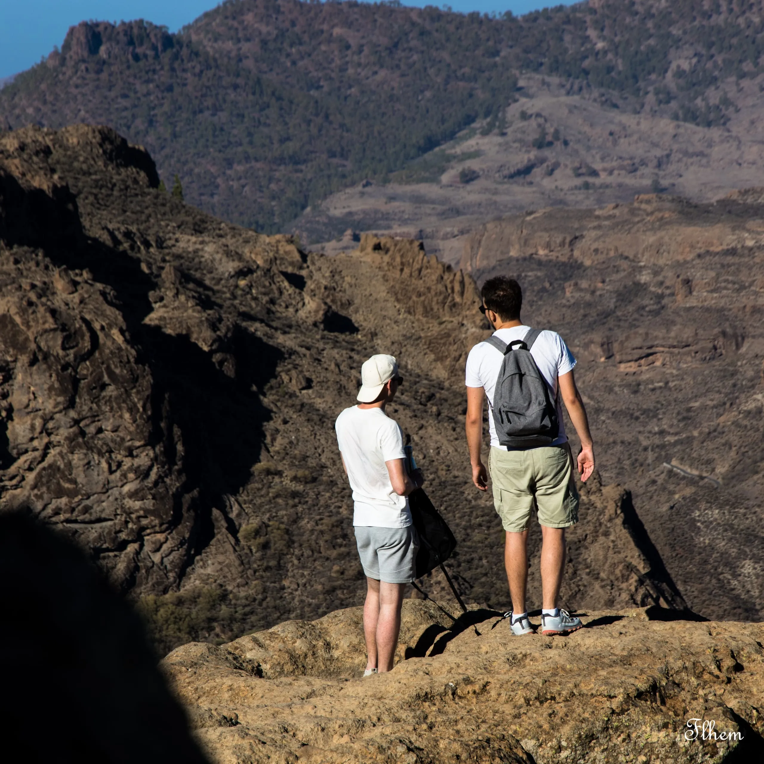 Deux randonneurs de dos au bord d'un promontoire rocheux, face à un vaste cirque montagneux