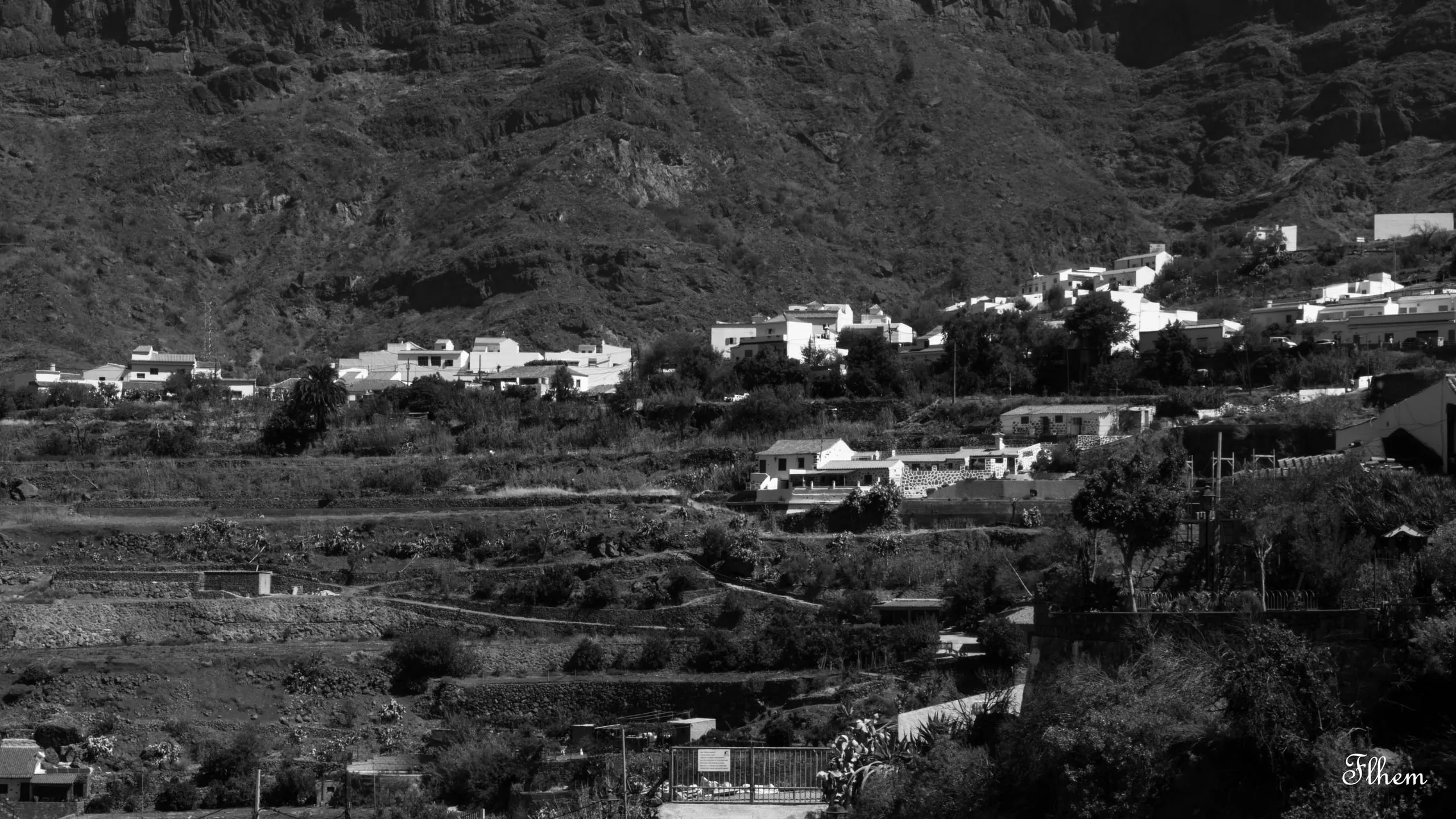 Village blanc accroché au flanc d'une vallée en terrasses, en noir et blanc