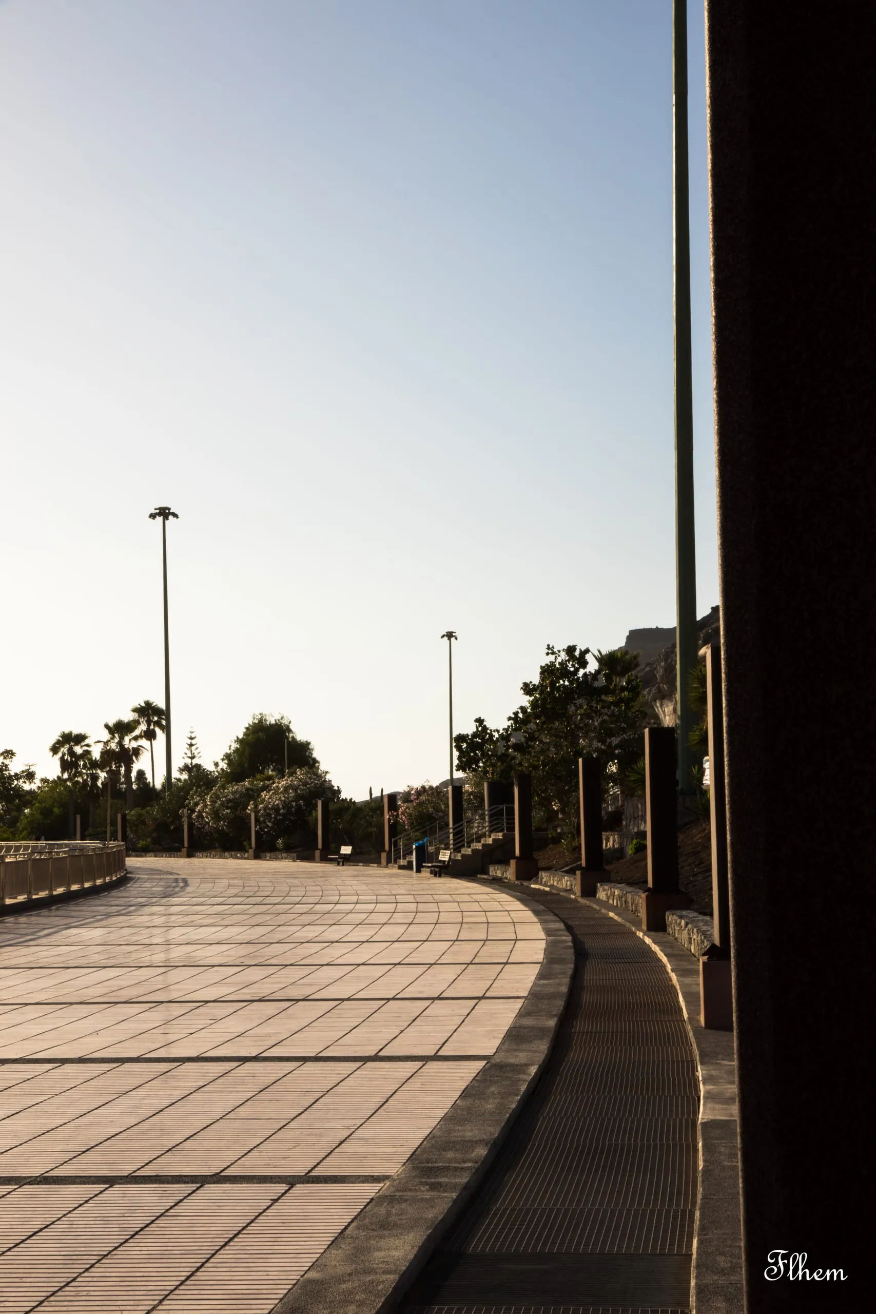 Promenade dallée en courbe bordée de lampadaires, vue depuis l'ombre d'un mur