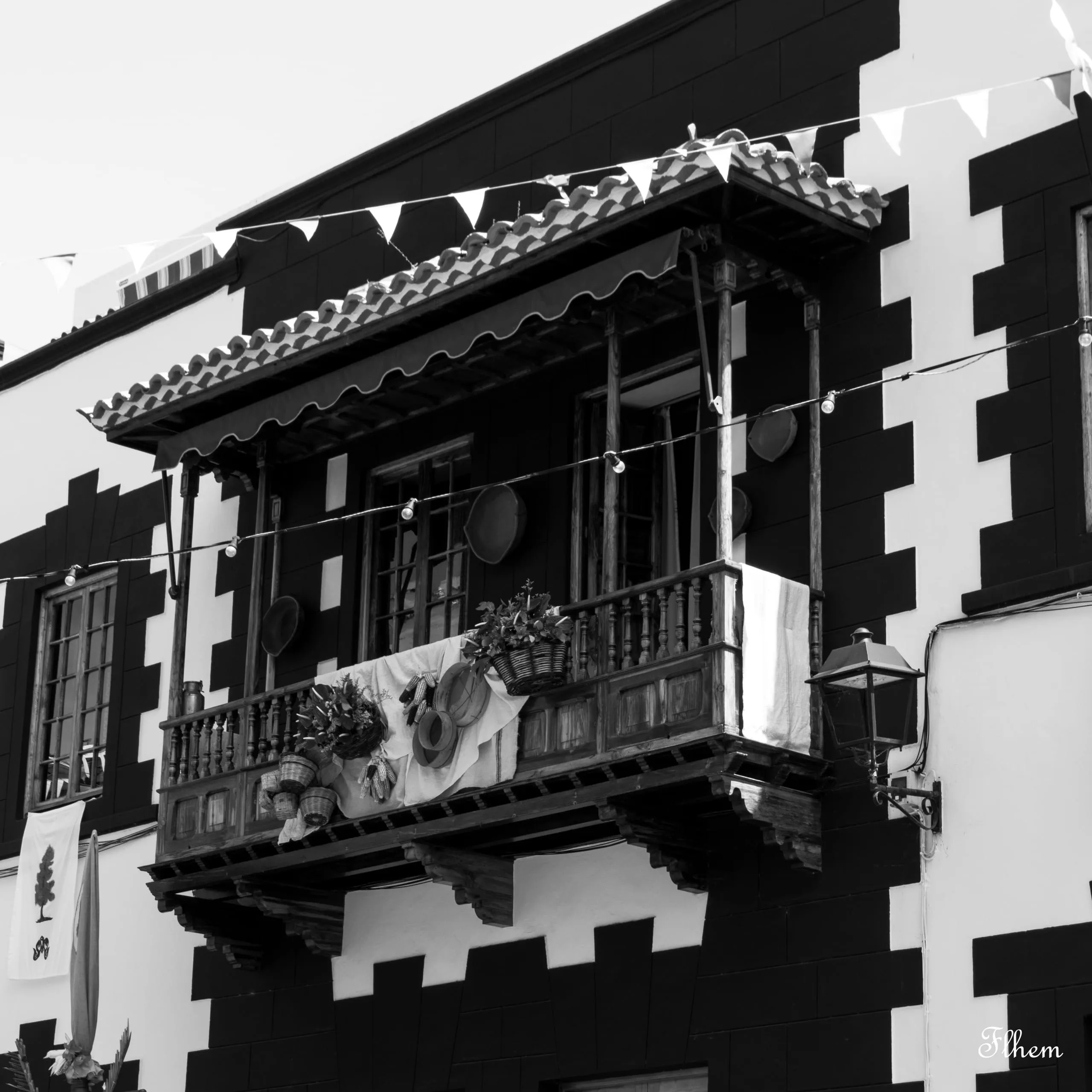 Balcon en bois sculpté sur une façade aux angles crénelés, fanions tendus, en noir et blanc